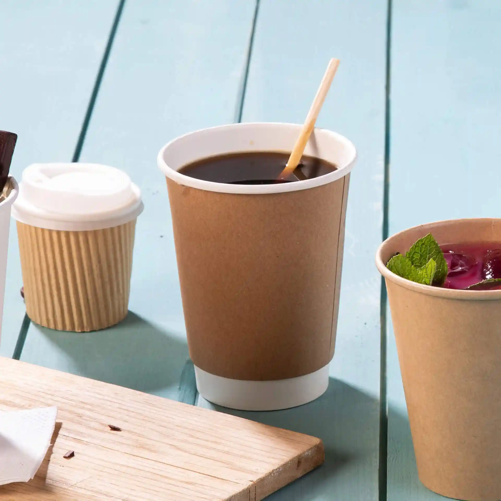 Brauner doppelwandiger Pappbecher mit weißem Innenfutter, gefüllt mit schwarzem Kaffee und einem Holzrührer.