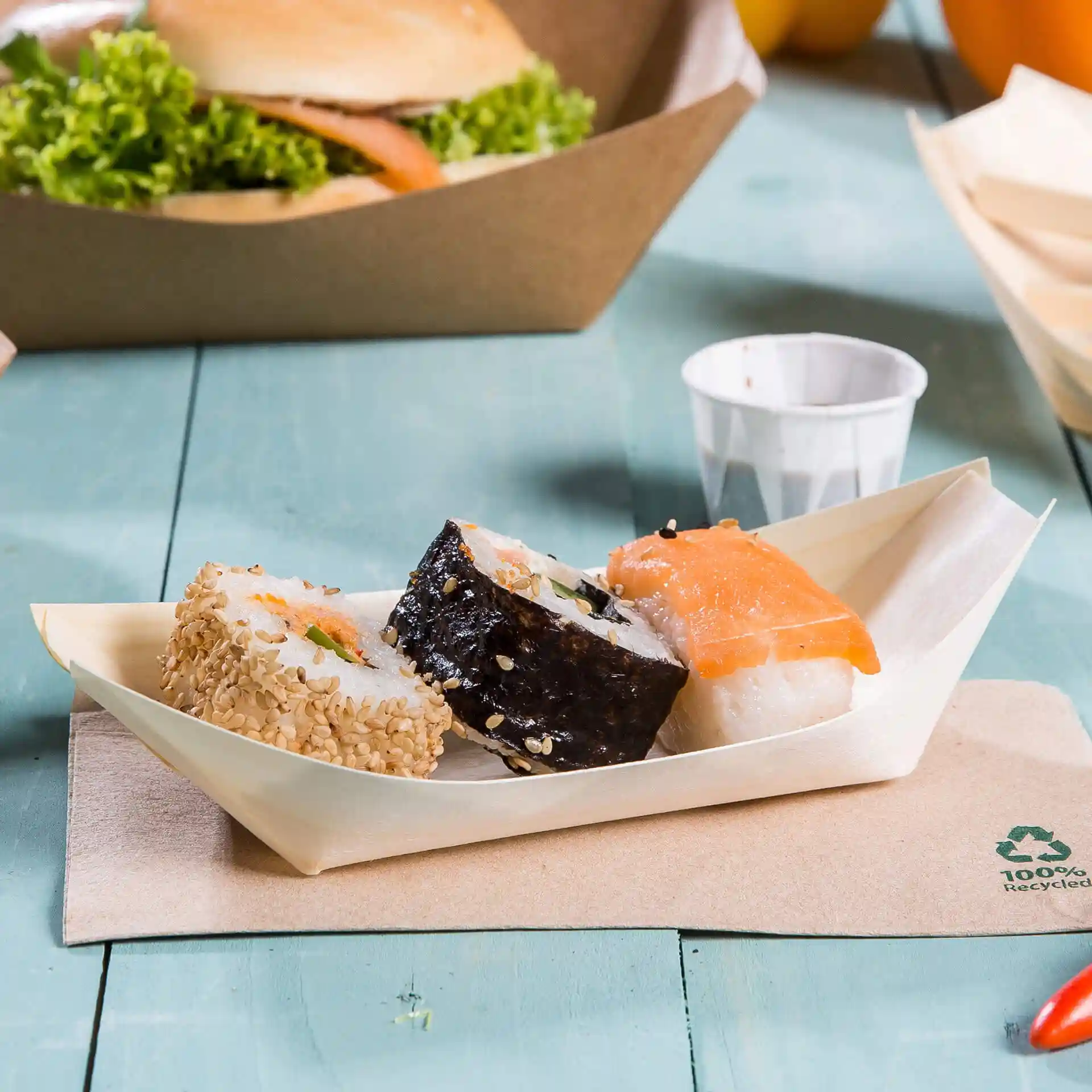 Three pieces of sushi served in a wooden boat-shaped tray on a light blue surface.