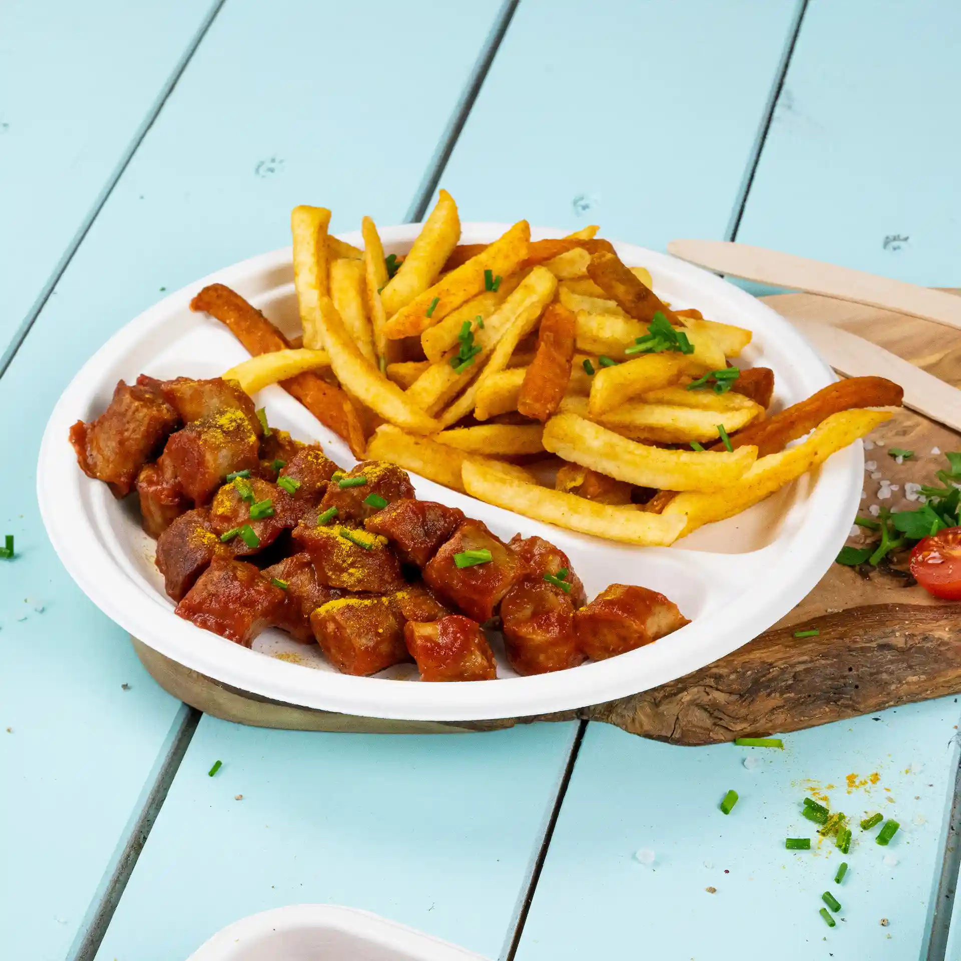 Runder weißer Zuckerrohr-Teller mit zwei Fächern, eines gefüllt mit gewürfeltem Fleisch in Sauce und das andere mit Pommes.