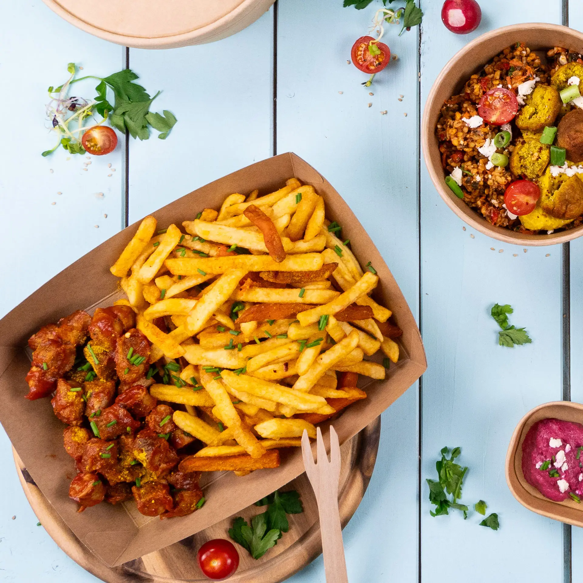A cardboard tray filled with golden French fries and spicy meatballs, accompanied by a small bowl of salad.