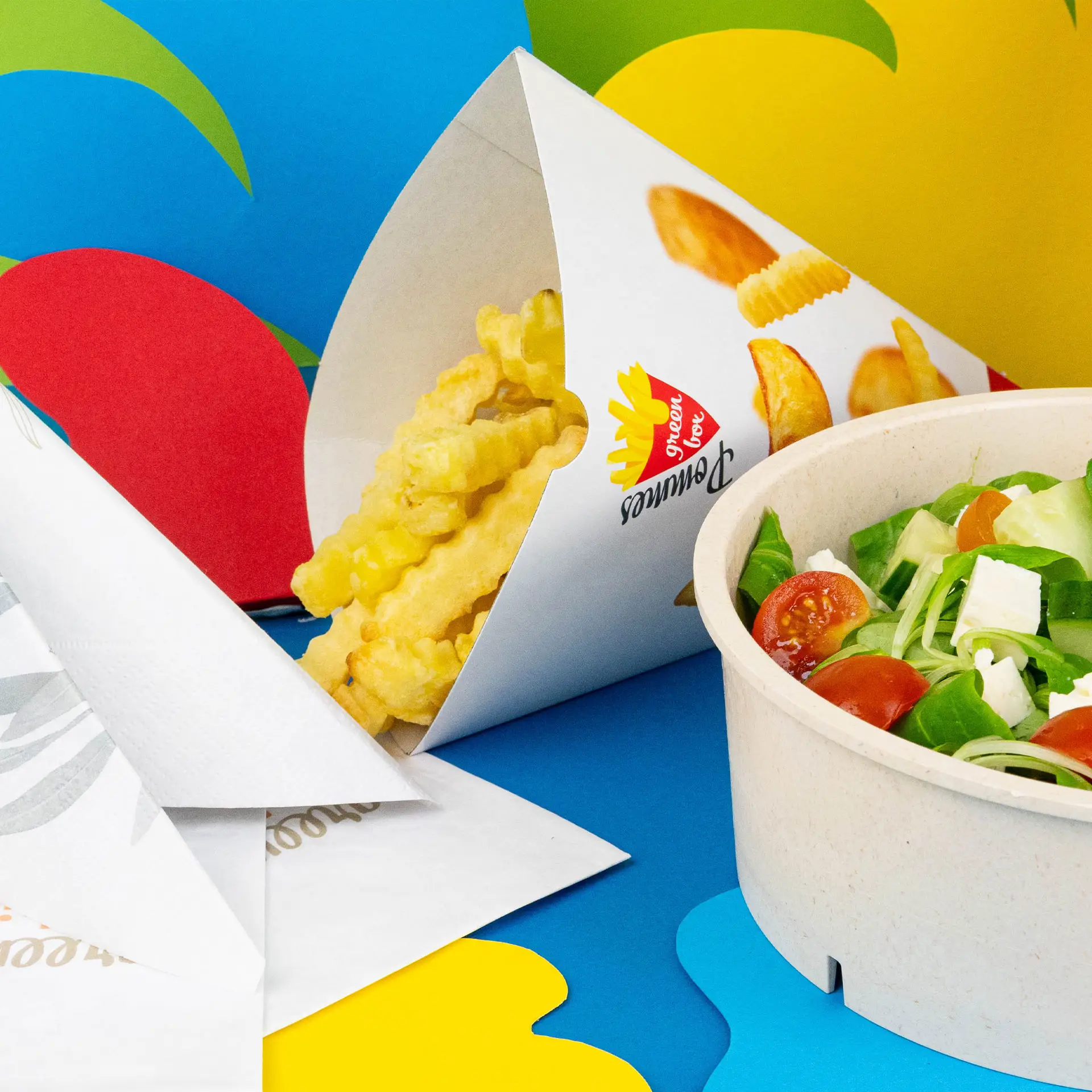 Ein bedruckter Snackbecher mit knusprigen Pommes und einem Salat in einer Schüssel auf einem bunten Hintergrund.