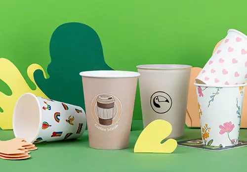 Various coffee cups displayed on a light blue surface, featuring different designs and labels, including "Alma & Auer" and "Indie Roasters."