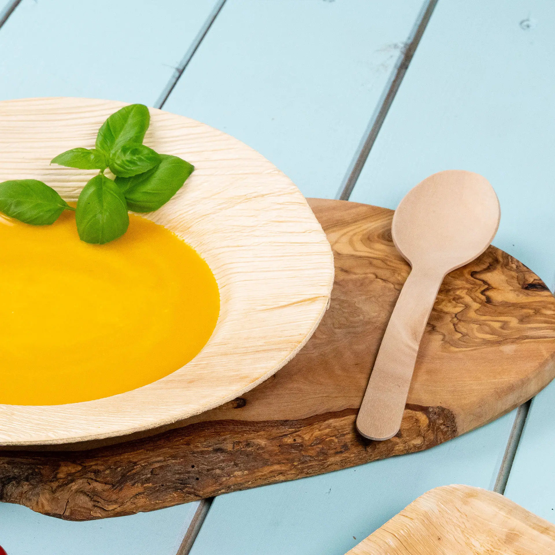 Bowl with yellow soup and a basil leaf, accompanied by a wooden spoon on a wooden serving board.
