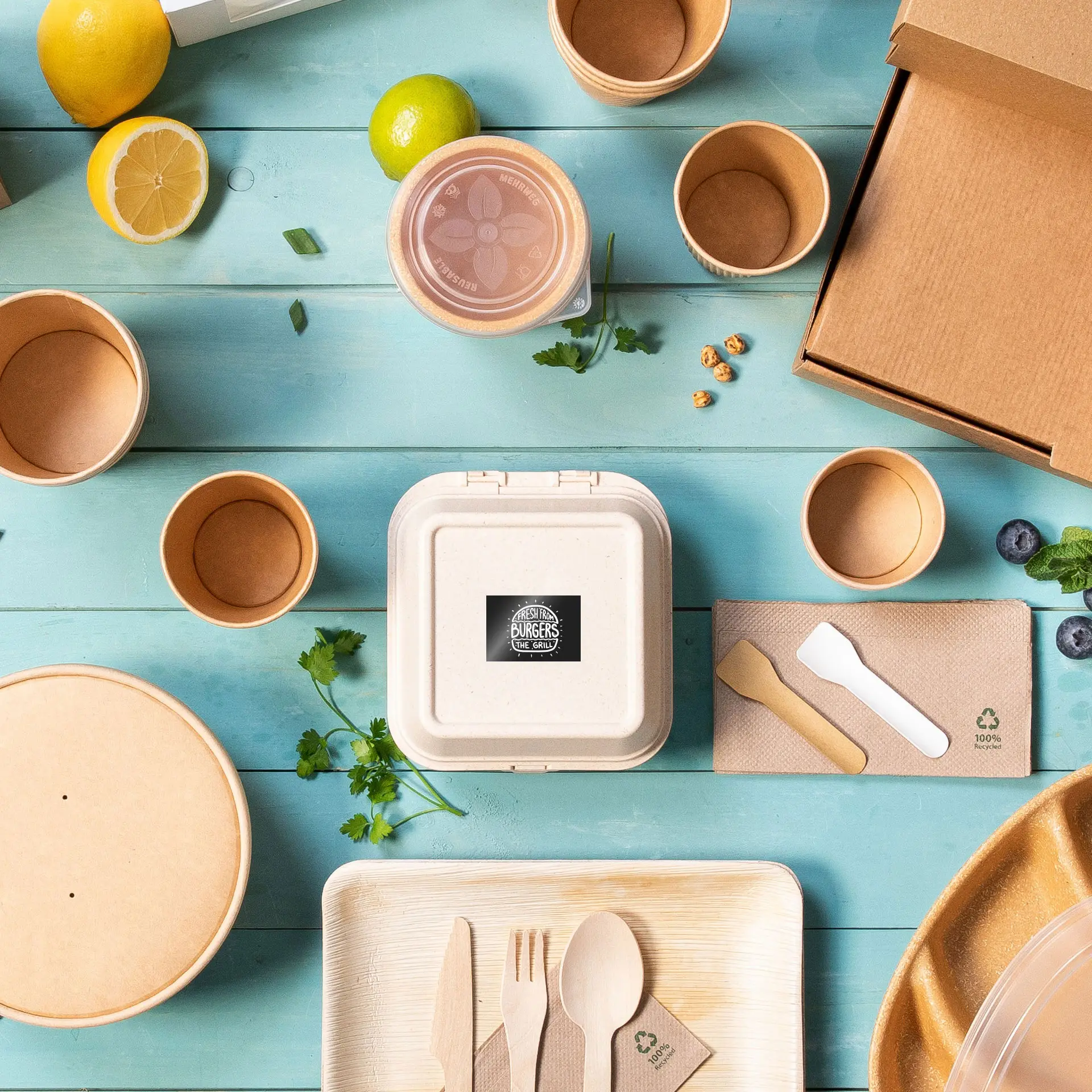 Various disposable containers, utensils, and food items arranged on a blue wooden surface with herbs and citrus fruits.