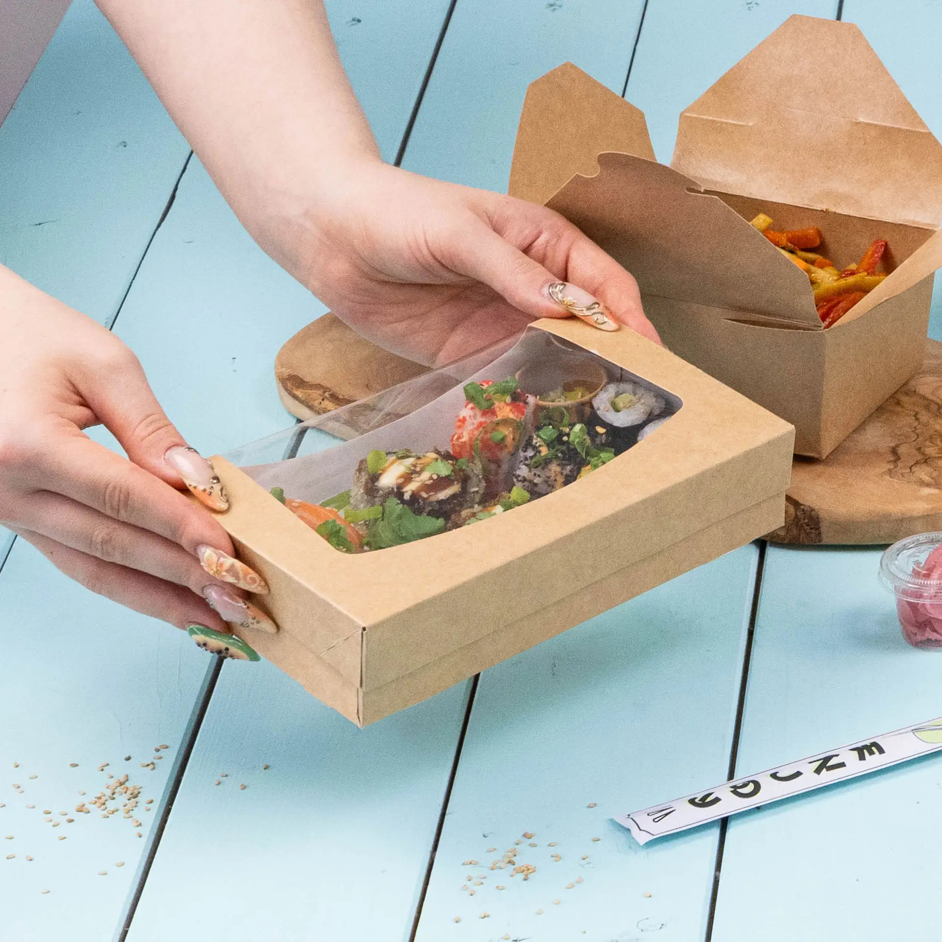 A windowed cardboard box containing a sandwich with cream cheese, spinach, and a fruit spread, placed on a teal surface.