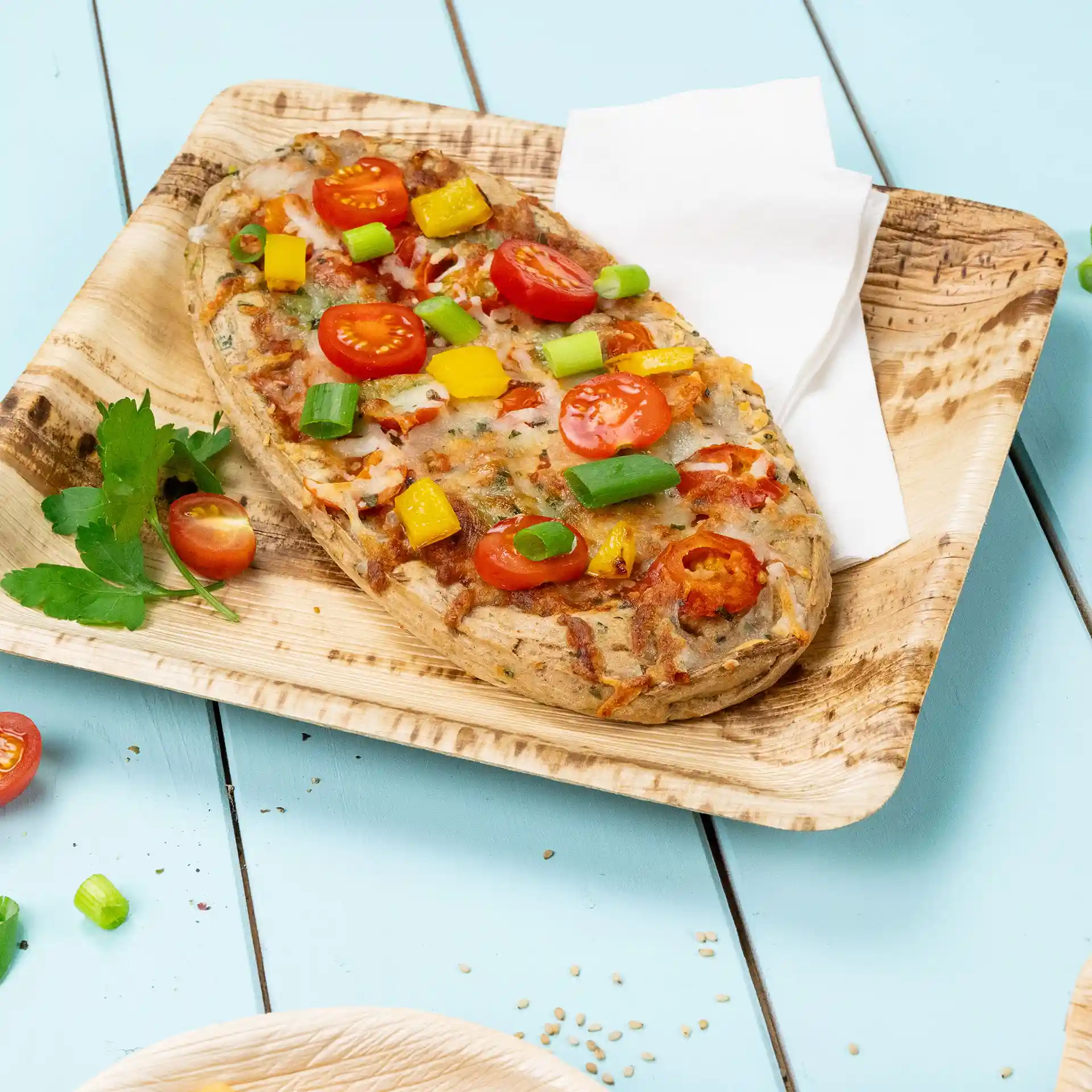Square palm leaf plate with a baked dish topped with cherry tomatoes, bell peppers, and green onions.