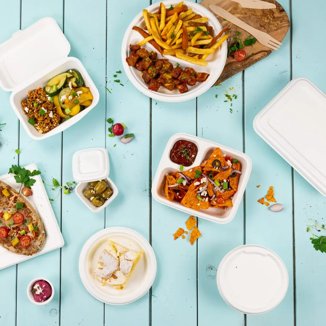 Verschiedene Lebensmittel in Takeout-Behältern auf einer blauen Holzoberfläche, darunter Pommes, Nachos und ein Dessert.