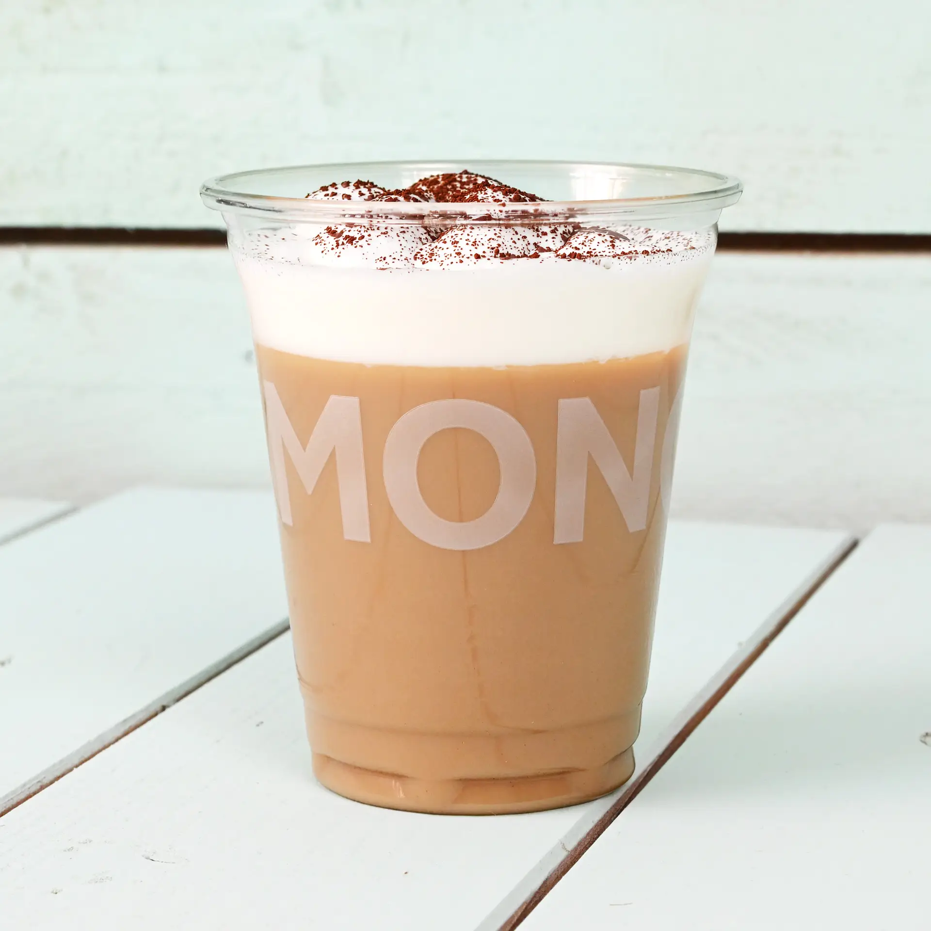 Klarer 16 oz rPET-Becher, gefüllt mit Eiskaffee, garniert mit Schlagsahne und Kakaopulver, auf einer weißen Holzoberfläche platziert.