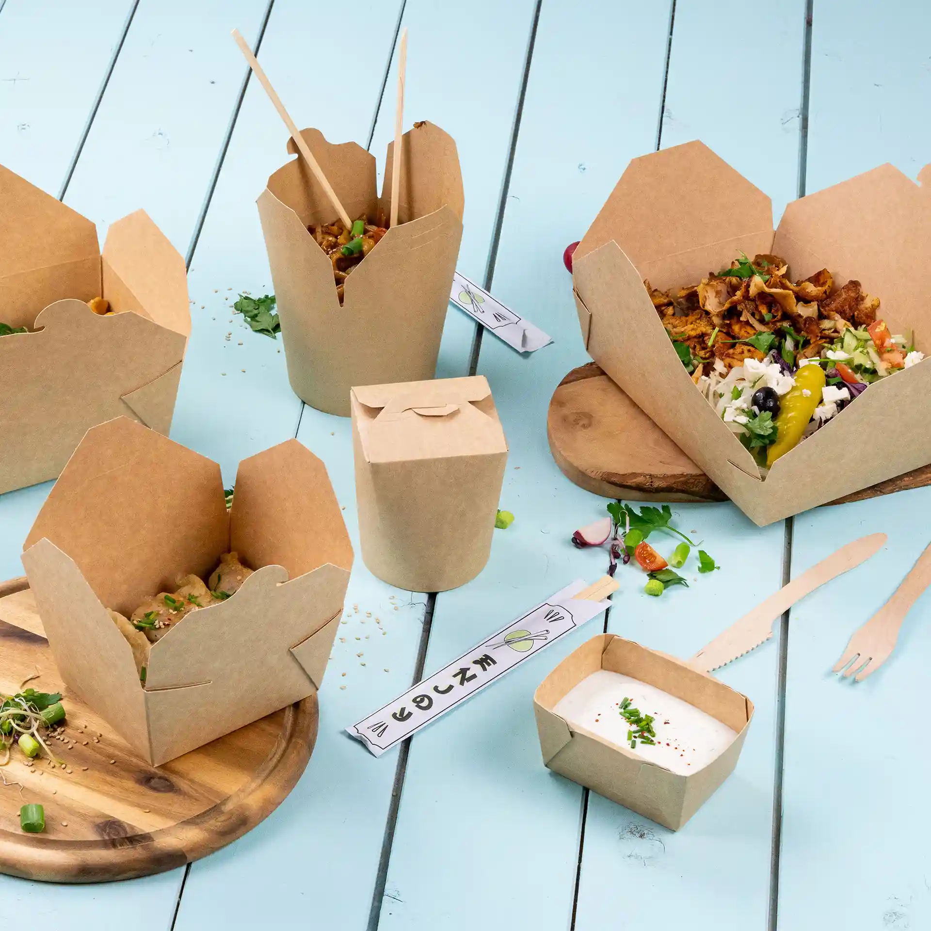Image of brown takeaway containers with various food items, including a sauce container, on a blue wooden surface.