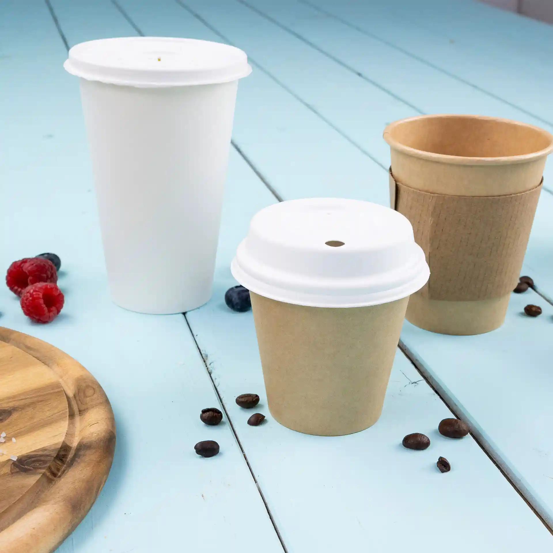 Image of three paper cups: one white single wall cup with a lid, one brown cup with a lid, and one brown cup without a lid, on a blue surface.