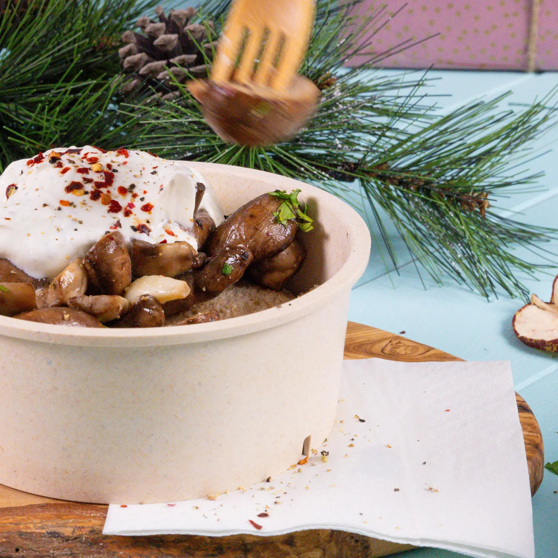Schüssel mit Pilzen und Joghurt, gewürzt, auf einem Holzbrett mit einer weißen Serviette daneben.