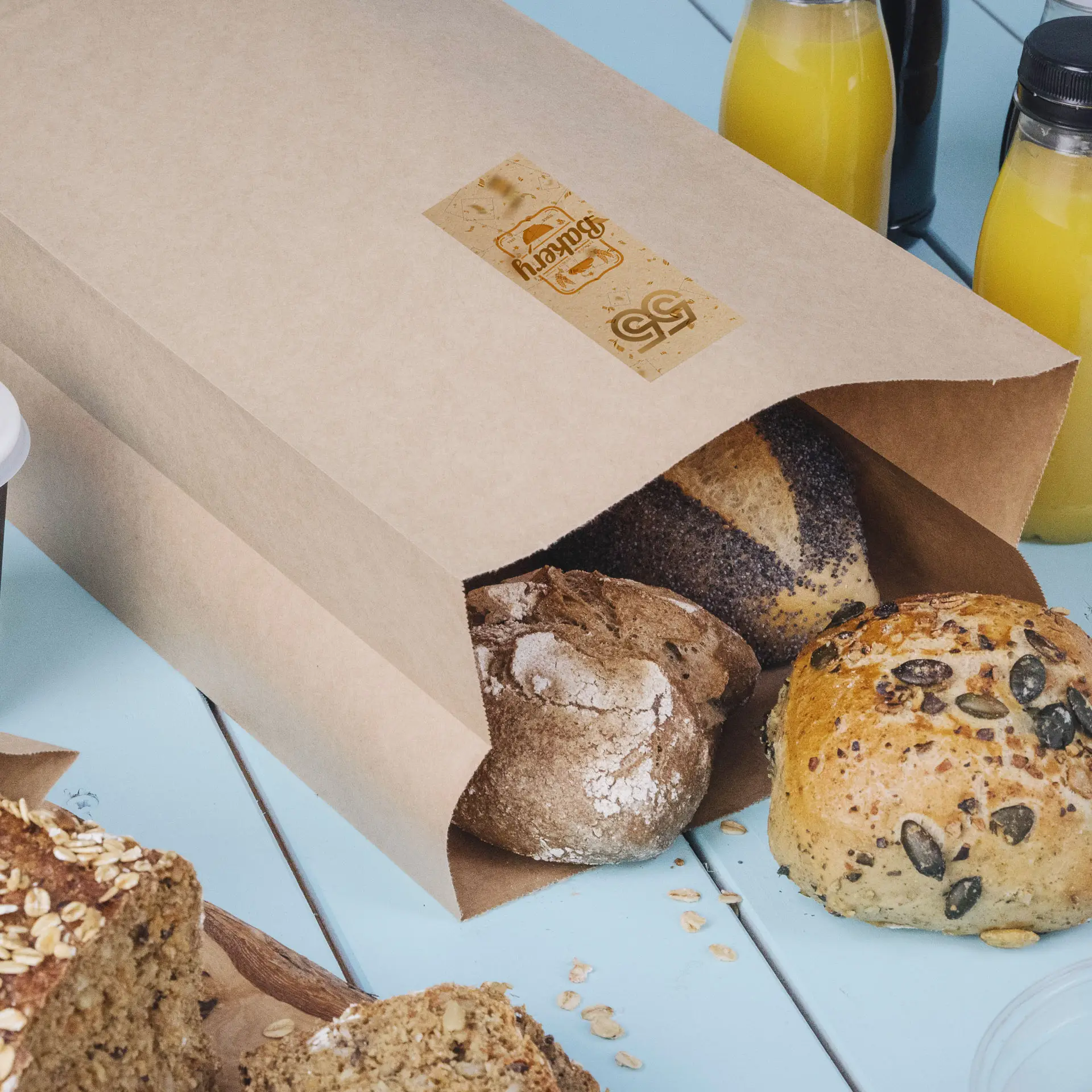 Brown kraft paper bag partially open with assorted breads visible, including a round roll and a loaf, on a light blue surface.
