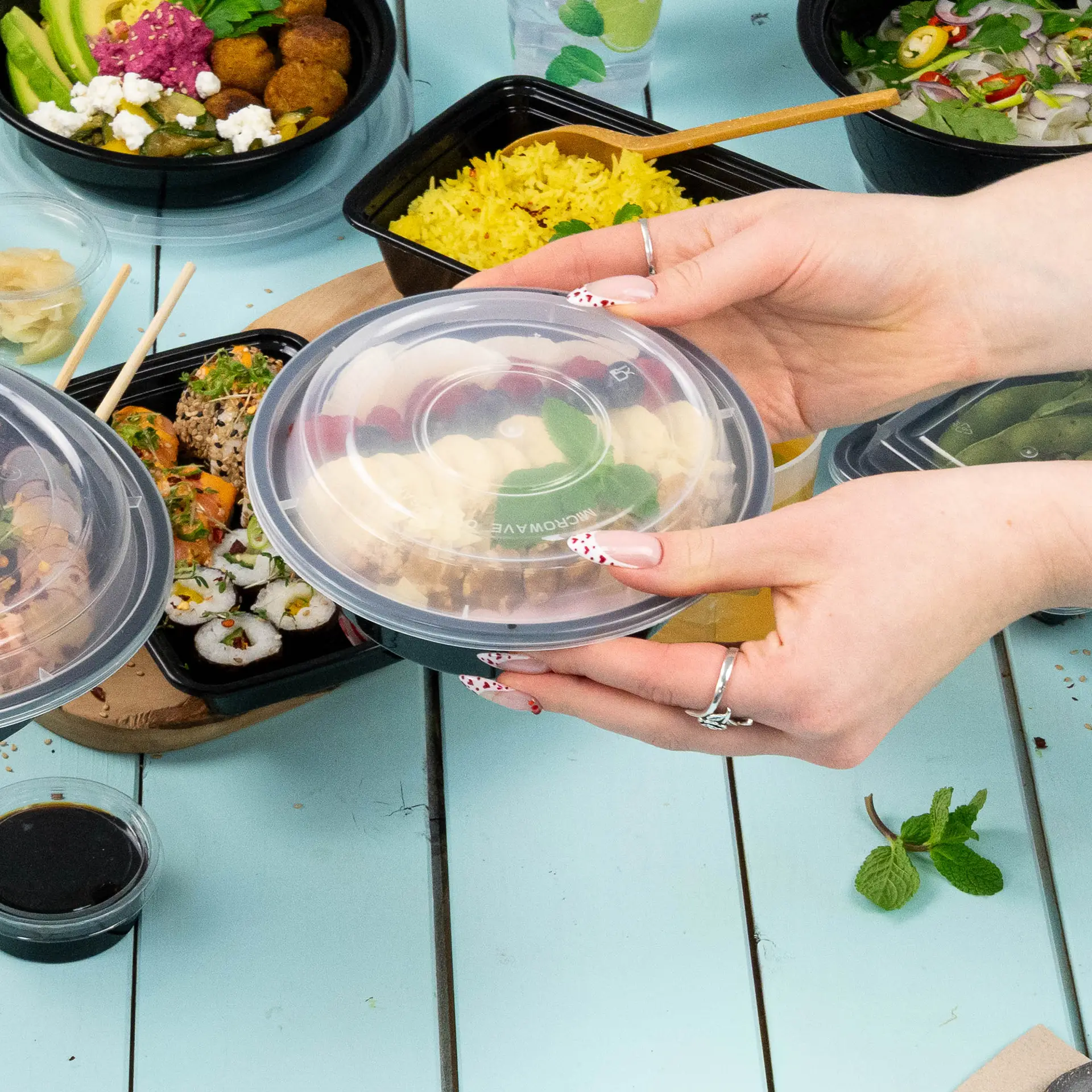 Transparent reusable lid for food containers; hands holding a lid above various meal dishes on a table.