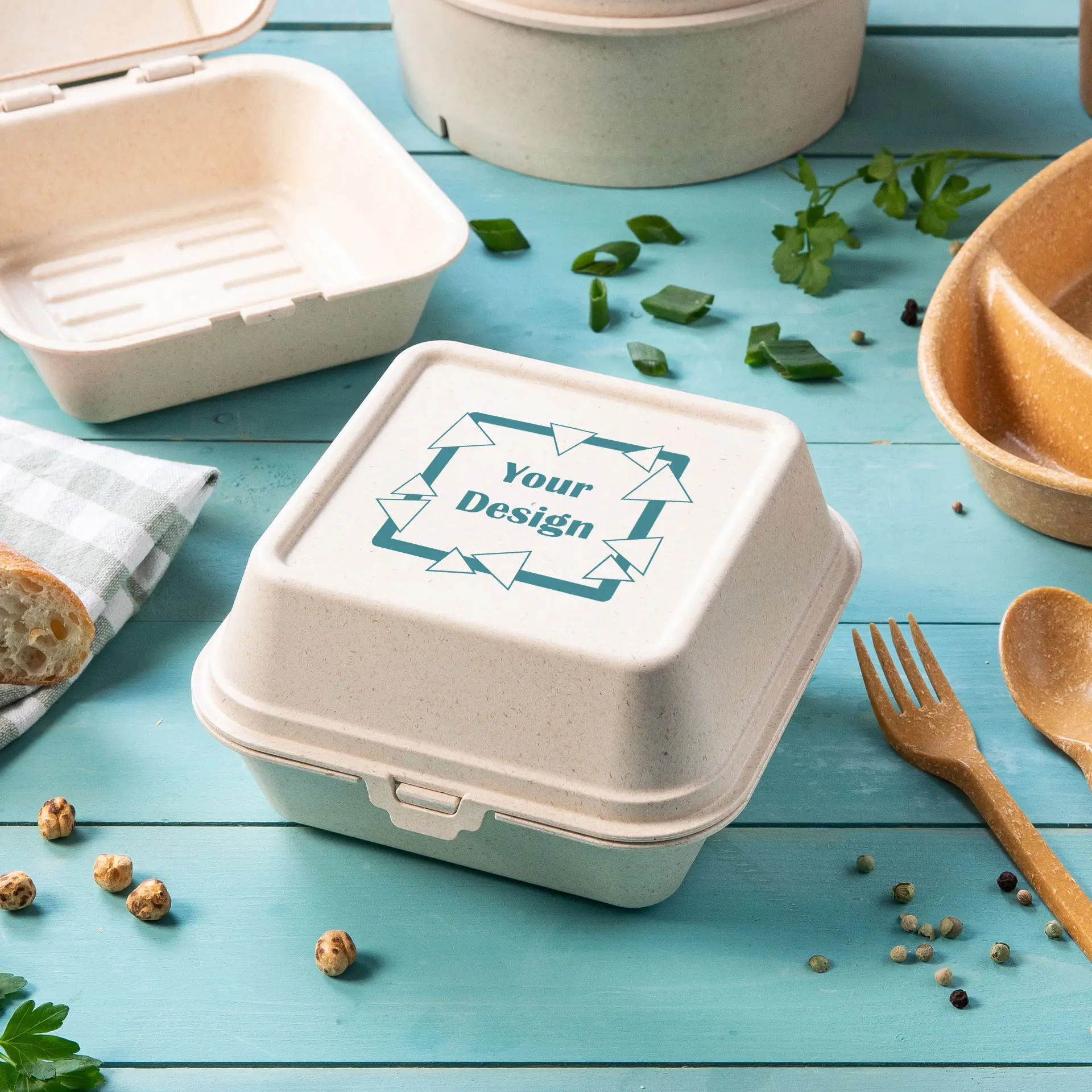 Wiederverwendbare Burgerbox aus Holz-Bio-Verbundstoff mit anpassbarem Deckel, umgeben von Lebensmitteln und Besteck.