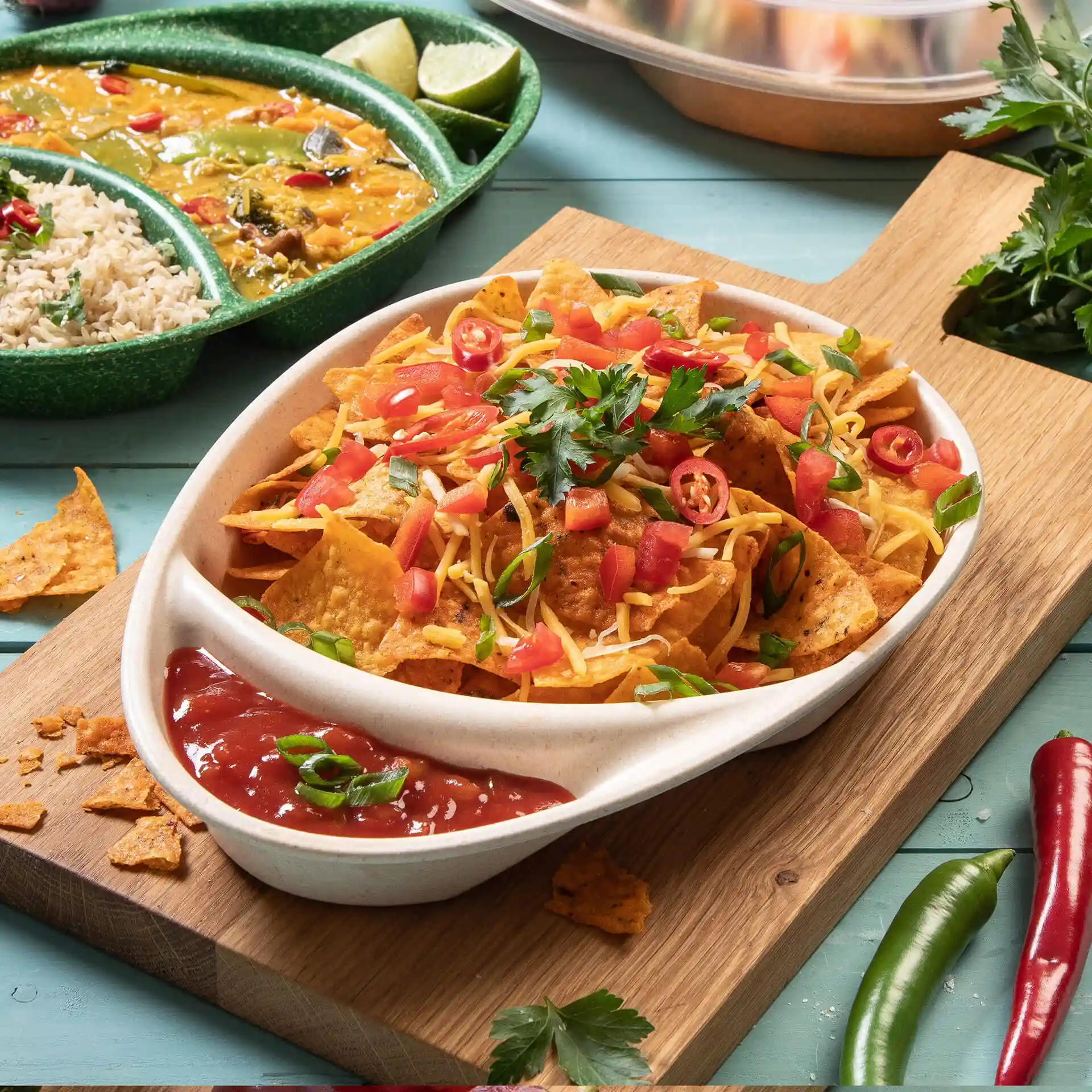 Gericht mit Nachos, belegt mit Käse, Tomaten und Koriander, serviert mit Salsa auf einem weißen, geteilten Teller.