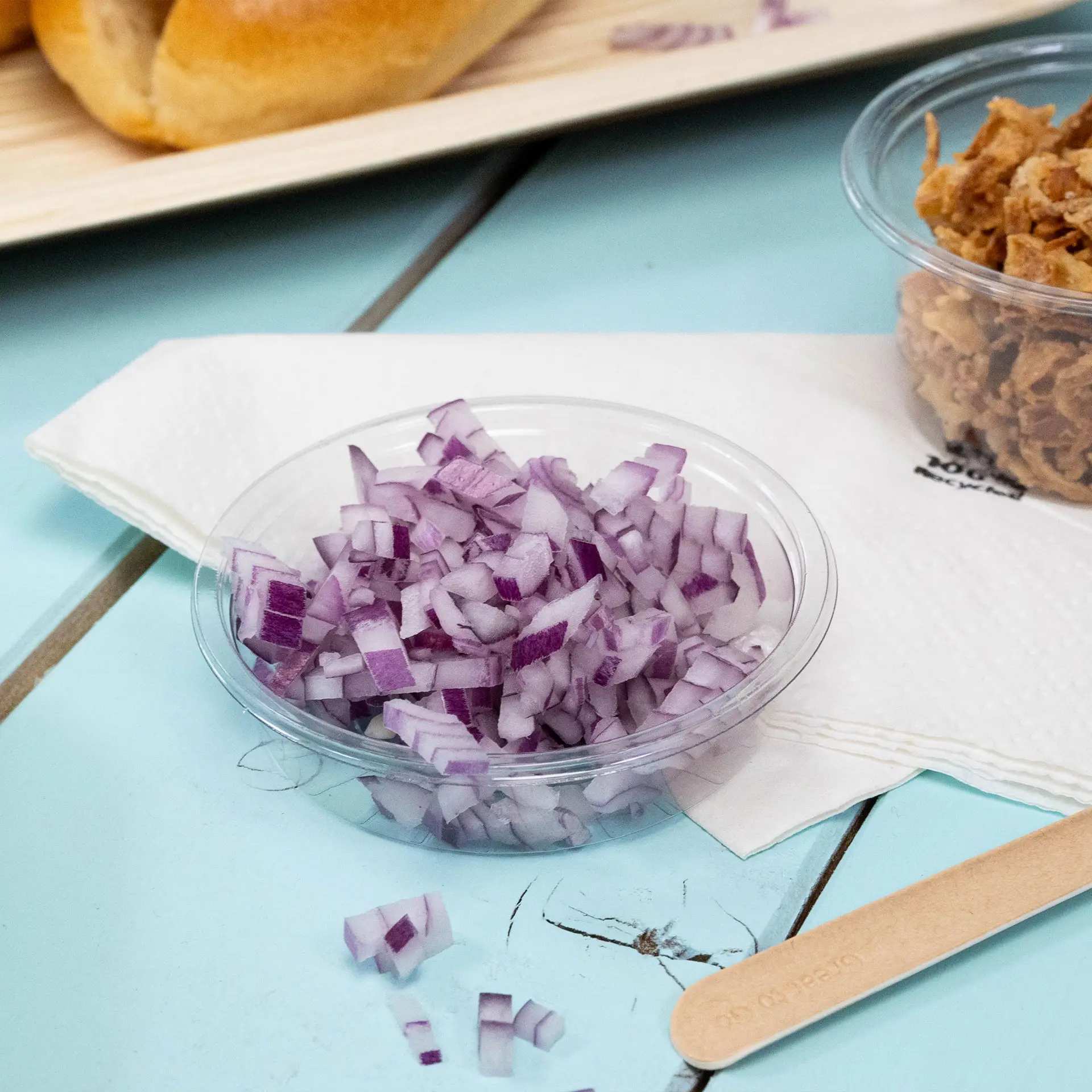 Hacken rote Zwiebeln in einem klaren Becher auf einer blauen Oberfläche, mit einer Serviette und einem Holzrührer daneben.