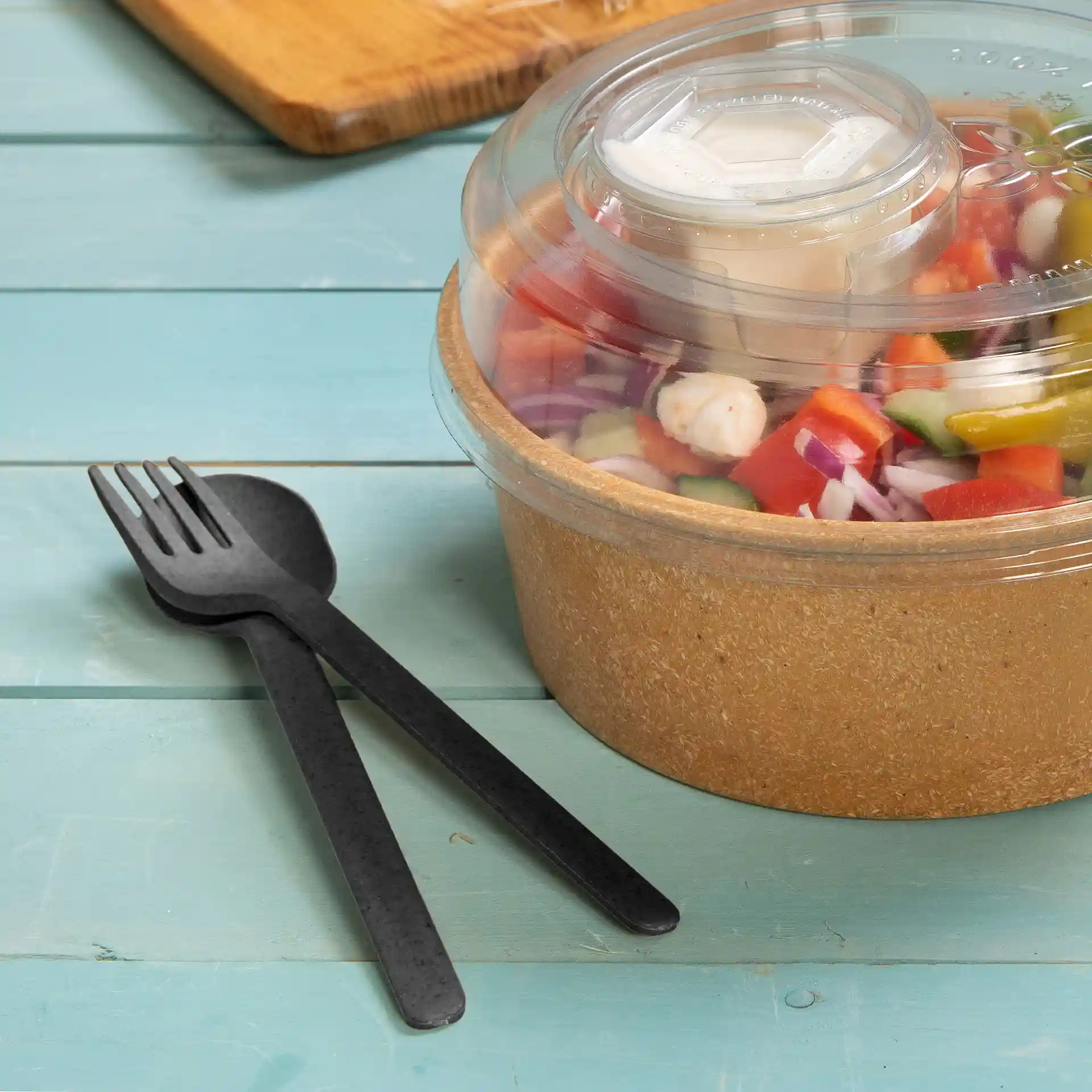 Schwarzes, wiederverwendbares Gabel- und Löffelset neben einer Salatschüssel mit klarem Deckel, gefüllt mit gemischtem Gemüse und Dressing.