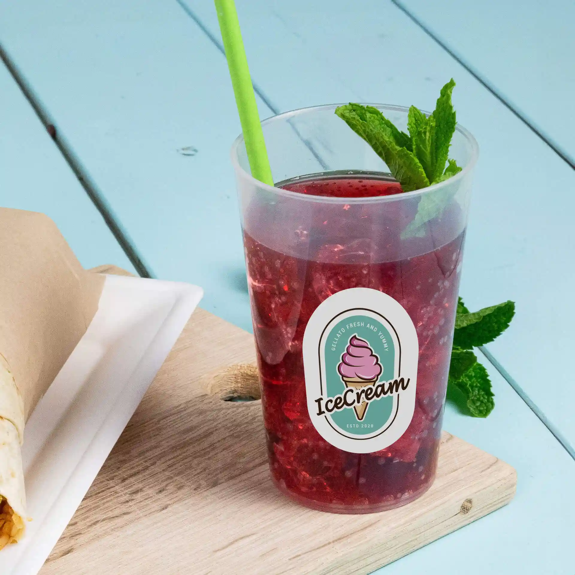 Clear reusable cup with a logo, filled with a red drink and a green straw, placed on a wooden surface.