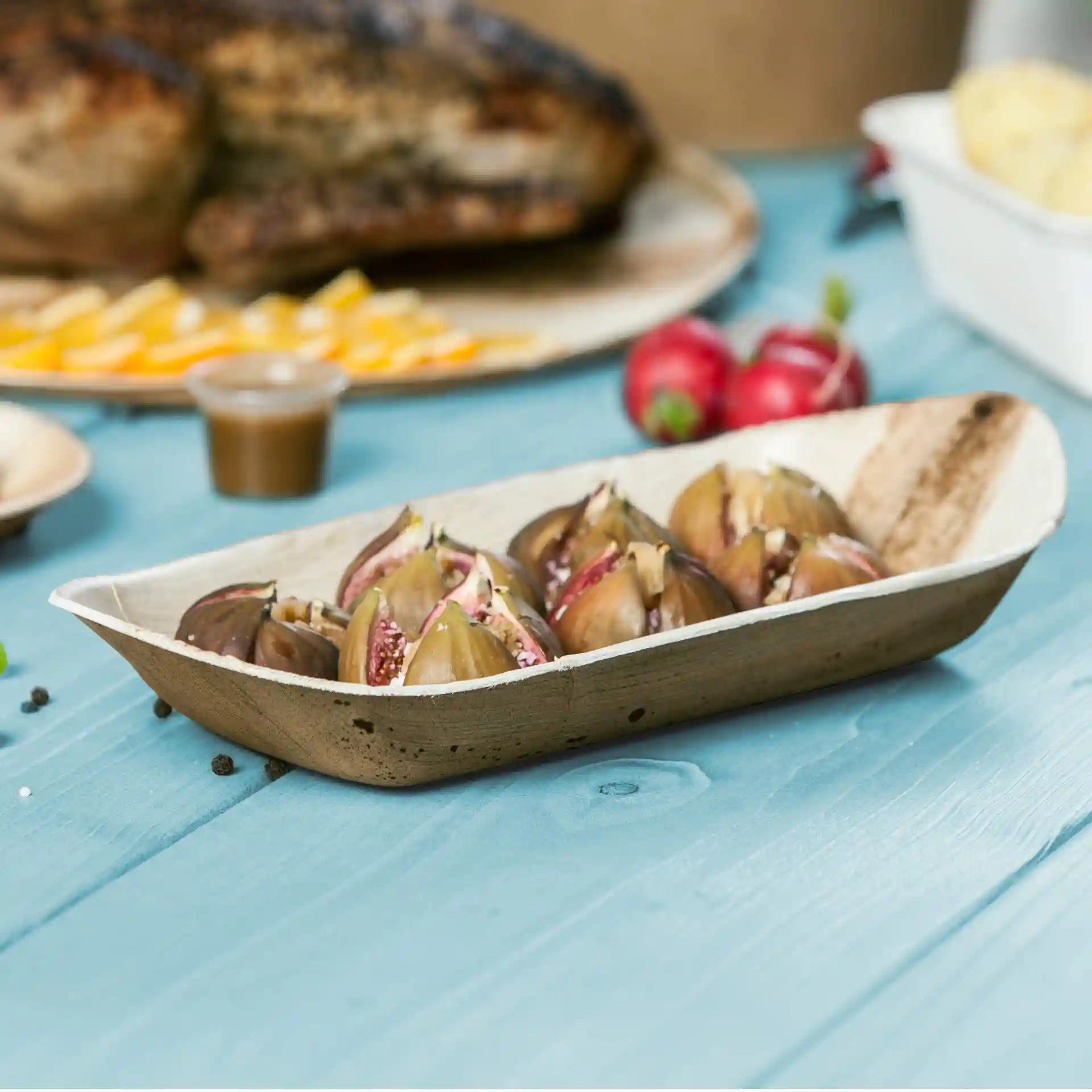 Deep palm leaf boat with several halved figs inside, placed on a blue wooden surface.