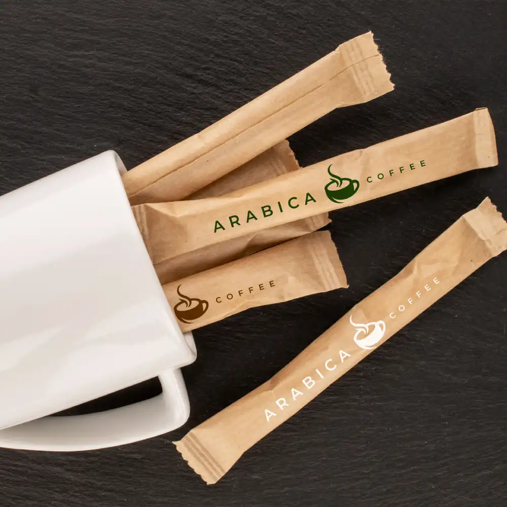 Brown sugar sticks labeled "ARABICA COFFEE" next to a white coffee cup on a dark surface.