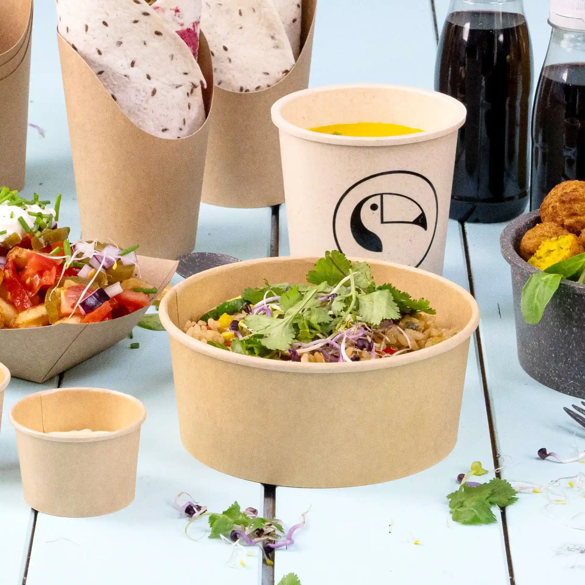Brown round paper bowl with eco-friendly coating, filled with food and garnished with herbs, on a blue surface.