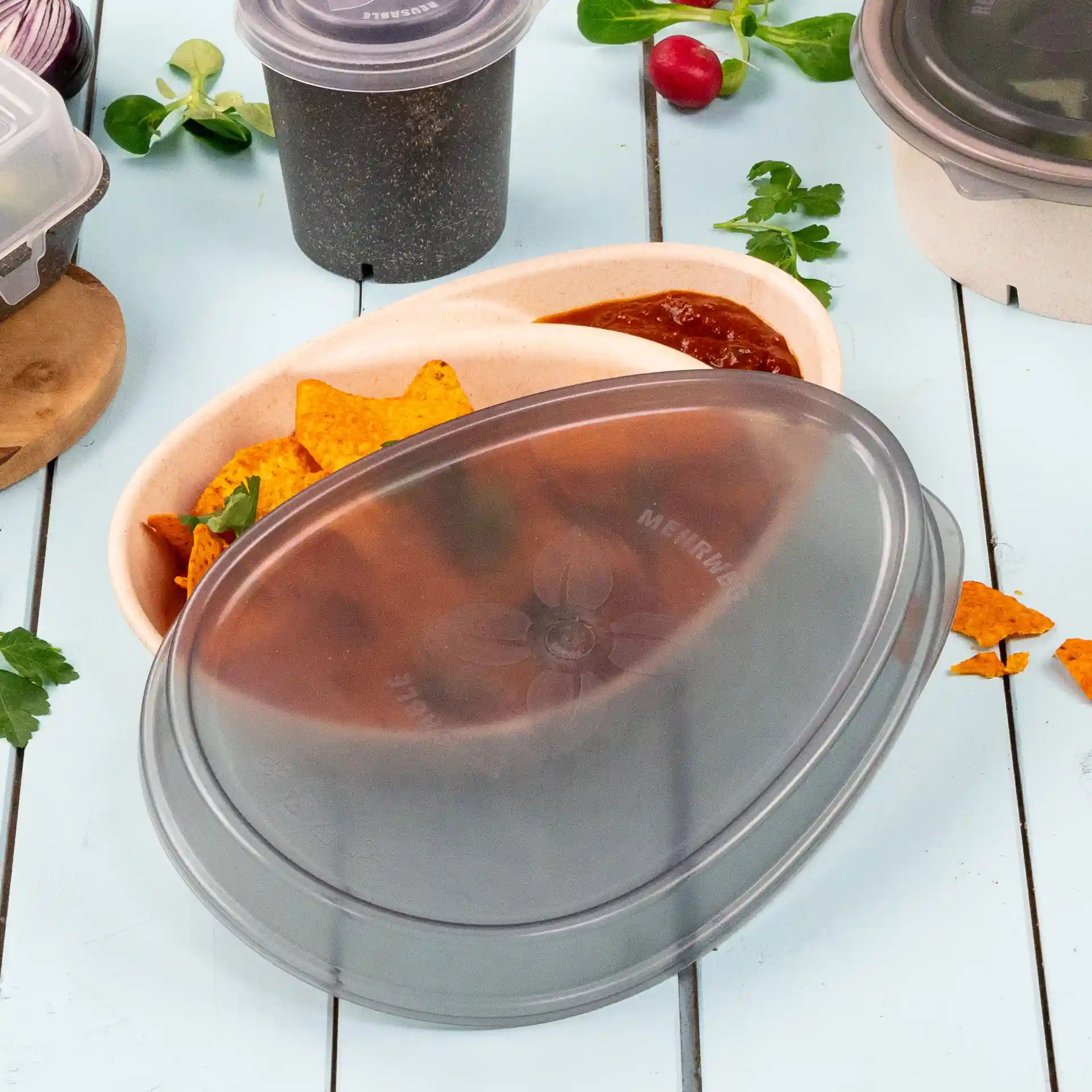 Grey oval reusable lid for a plate, shown with tortilla chips and salsa in a container, on a light blue surface.