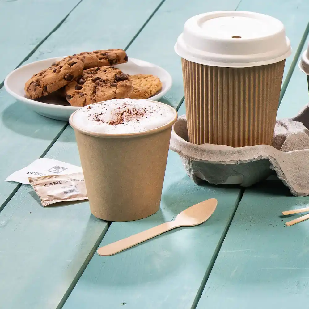 Brown coffee cup with foam and cocoa, cookie plate, wooden spoon, and cup holder on a blue wooden surface.