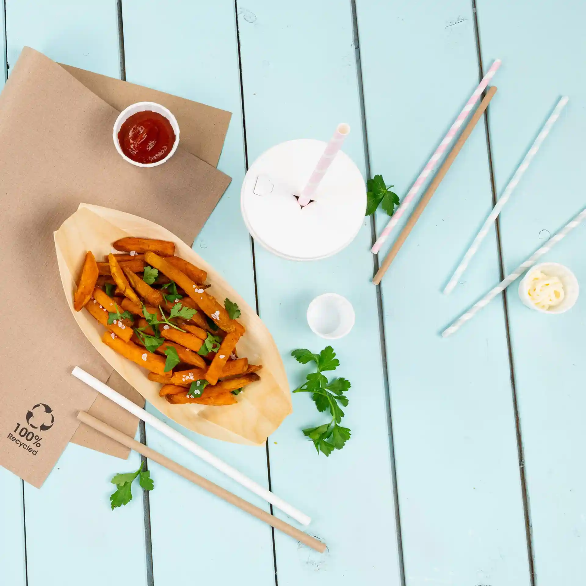 Image of sweet potato fries garnished with parsley, served in a wooden boat with ketchup, a drink cup, and paper straws.