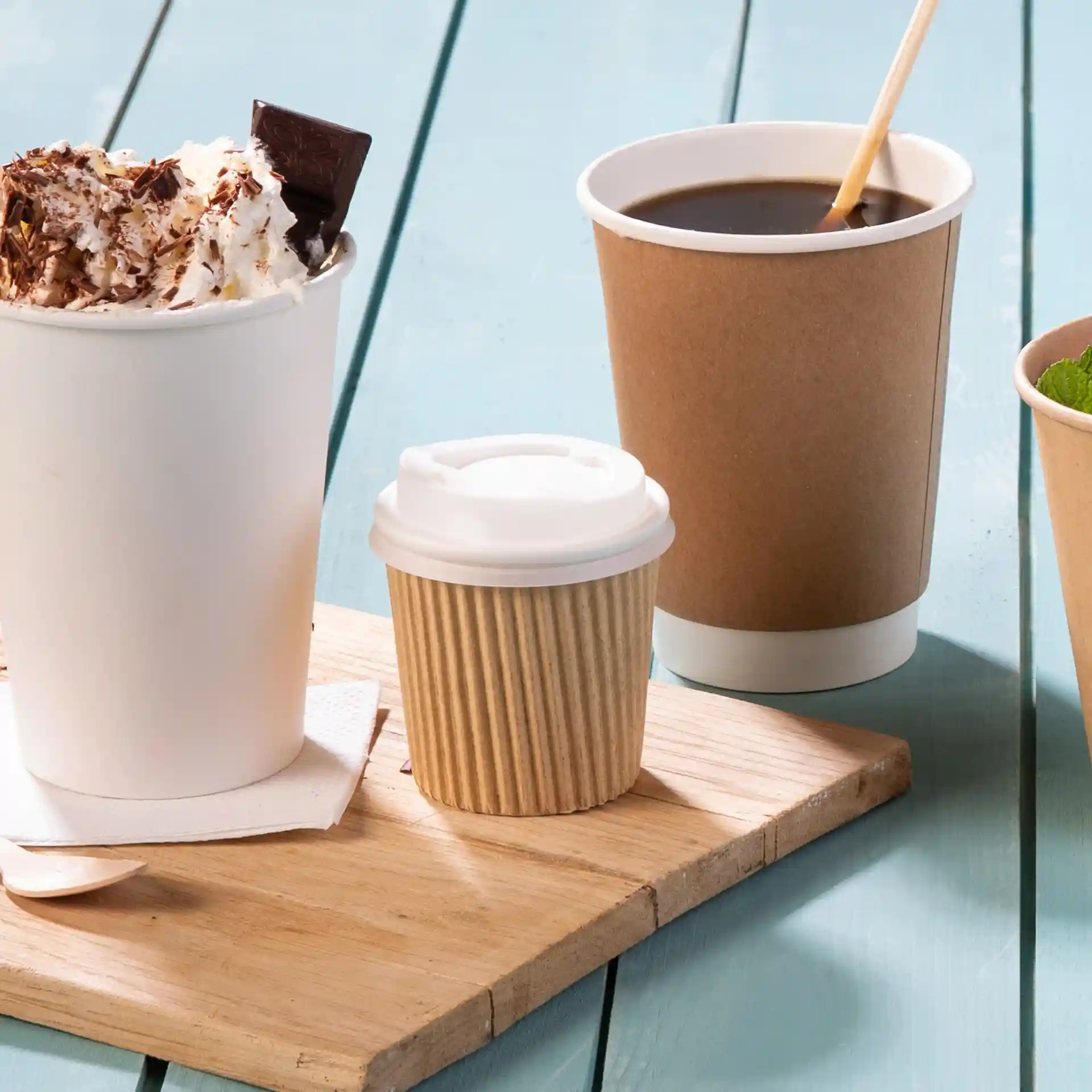 Bild von einem Holzbrett mit einer großen weißen Becher, bedeckt mit Sahne und Schokolade, einem kleinen gerippten braunen Becher und einem braunen Kaffeebecher.