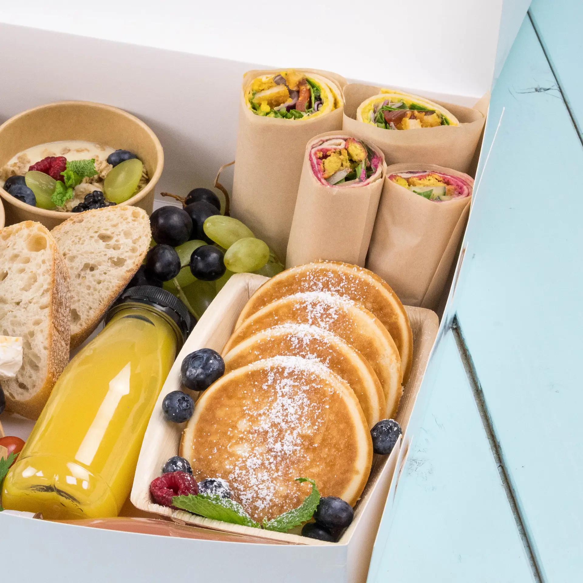Tablett mit Pfannkuchen, Gemüse-Wraps, Obst, Brot und einer Flasche Saft für den Einsatz im Service.