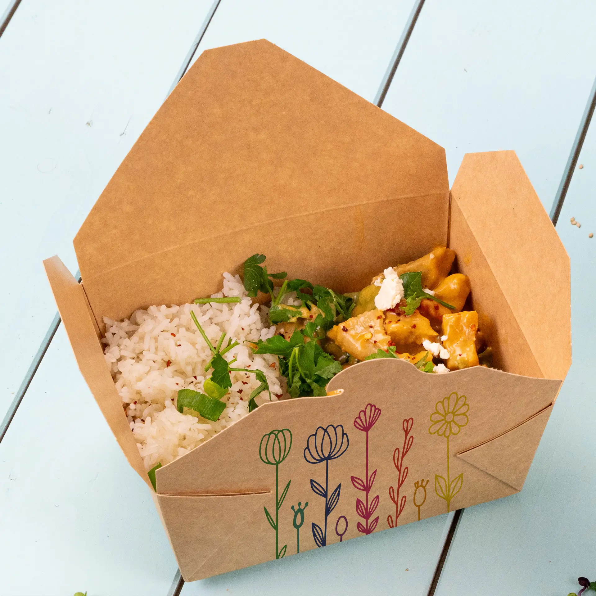 Takeaway box filled with rice and a curry dish, featuring floral design on the exterior.