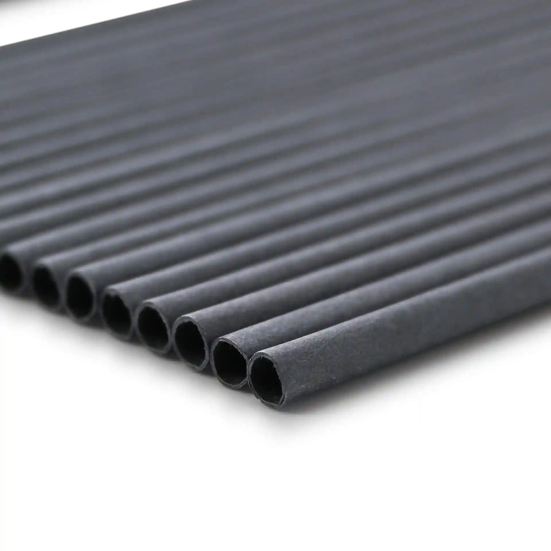 Schwarze Papierstrohhalme, 20 cm lang und 0,5 cm im Durchmesser, in einer Reihe auf einem schlichten Hintergrund angeordnet.