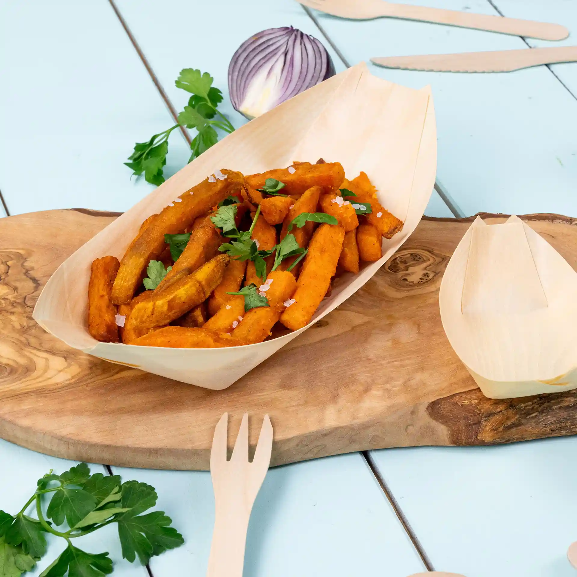 Holzboot-förmige Servierplatte mit Süßkartoffelpommes, garniert mit Petersilie, auf einer Holzoberfläche.
